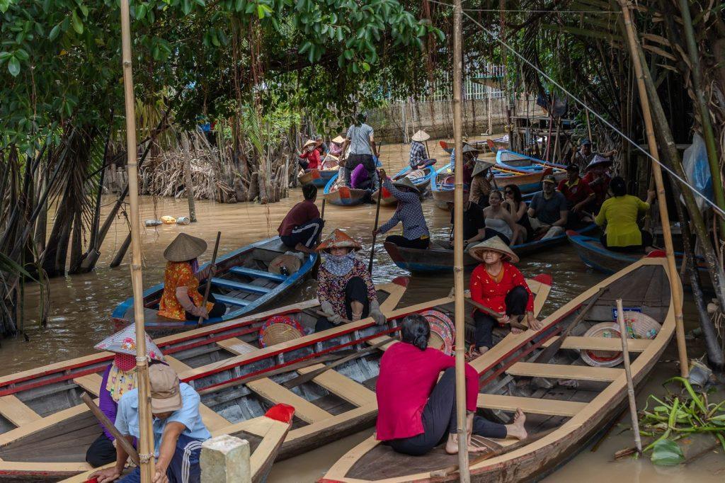 Locals and travelers sitting in wooden canoes on a canal in the Mekong Delta