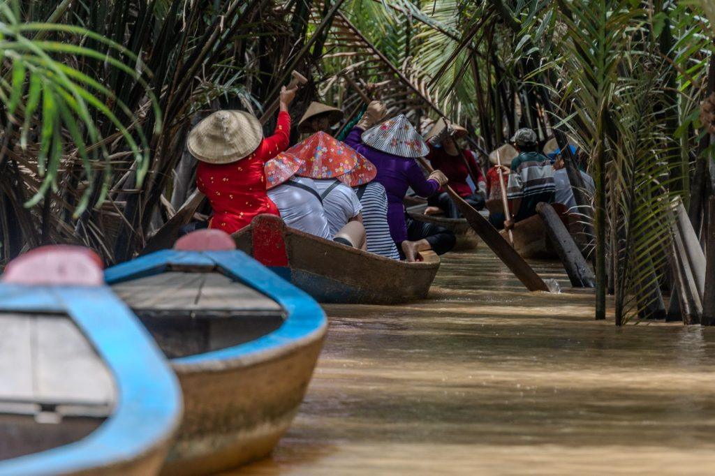 Visitors and rowers in dugout canoes navigating a narrow canal in the Mekong Delta in Vietnam