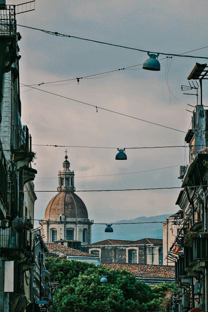 Dome of a church in Catania seen from a street lined with buildings.