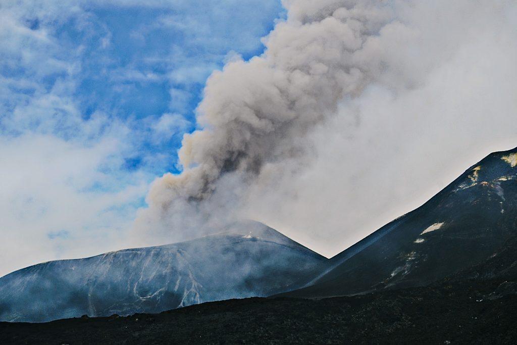 Panache de cendres s’élevant du cratère de l’Etna sous un ciel partiellement dégagé.