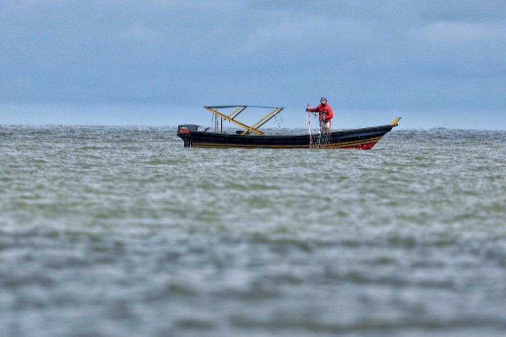 fisherman alone on a boat casting a net under gray clouds
