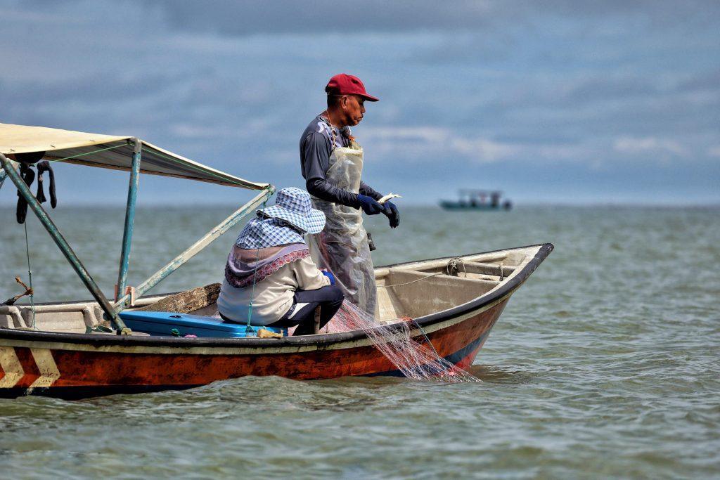 two fishermen on a small boat handling a net with clouds on the horizon