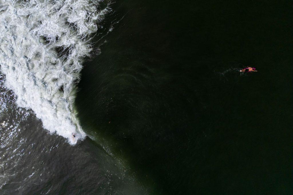 Surfeur ramant vers une vague tandis qu’une autre vague déferle à proximité.