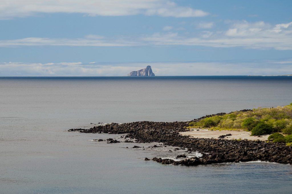 Coastal view of the Galapagos with a rocky island on the horizon and a beach lined with vegetation.