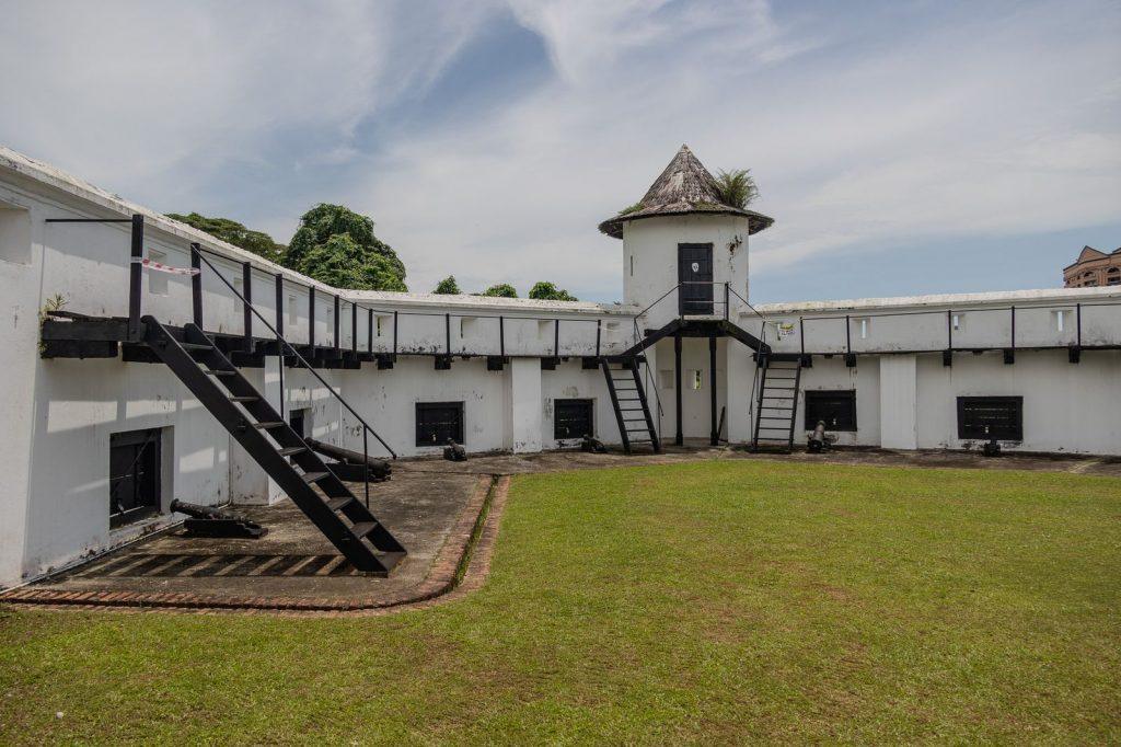 Cour intérieure du Fort Margherita à Kuching, avec escaliers en bois et anciennes pièces d’artillerie orientées vers le fleuve.