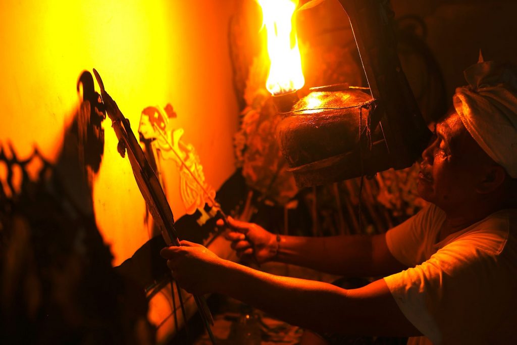 Dalang manipulant des marionnettes Wayang Kulit sous une lampe traditionnelle lors d’un spectacle à Bali.