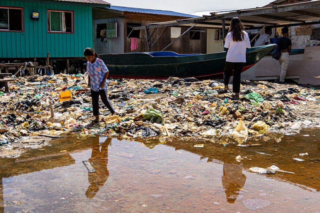 Enfants marchant parmi des déchets plastiques accumulés autour d’habitations dans un village côtier.