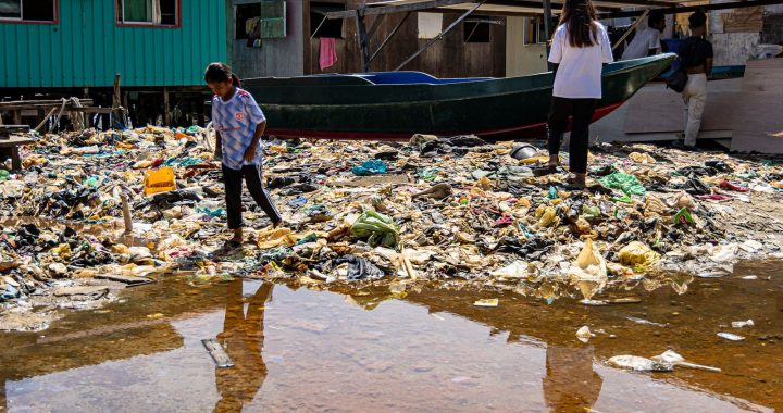 Enfants marchant parmi des déchets plastiques accumulés autour d’habitations dans un village côtier.