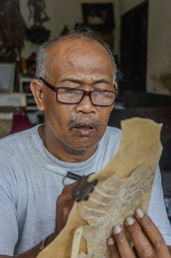 Portrait du Dalang concentré fabricant une marionnette Wayang Kulit dans son atelier.