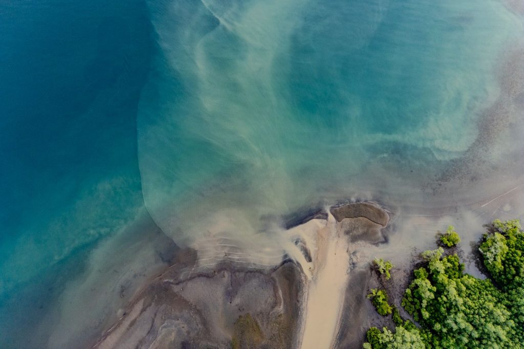 Vue aérienne d’une embouchure de rivière se jetant dans la mer avec mélange d’eaux claires et chargées.