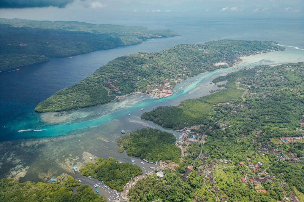 Vue aérienne d’une île côtière entourée de récifs et de zones peu profondes avec habitations.