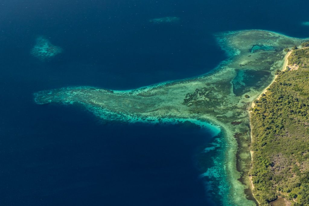 Vue aérienne d’un récif corallien longeant une côte avec dégradé de bleu .