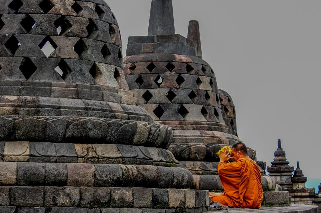 Moine bouddhiste assis devant les stupas du temple de Borobudur en Indonésie.
