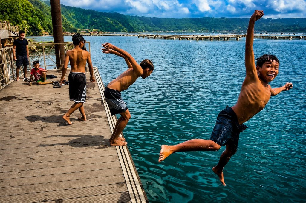 Enfants sautant depuis un ponton en bois dans un lac au bord d'un village.