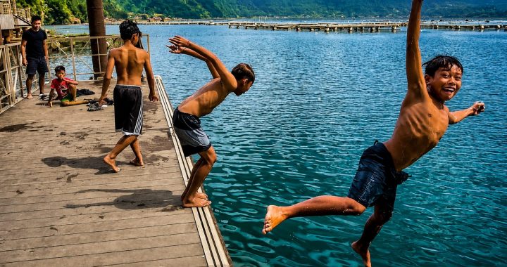 Enfants sautant depuis un ponton en bois dans un lac au bord d'un village.
