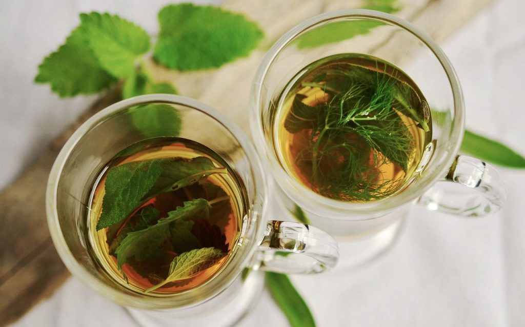Tasses de thé infusé avec des feuilles et herbes aromatiques.