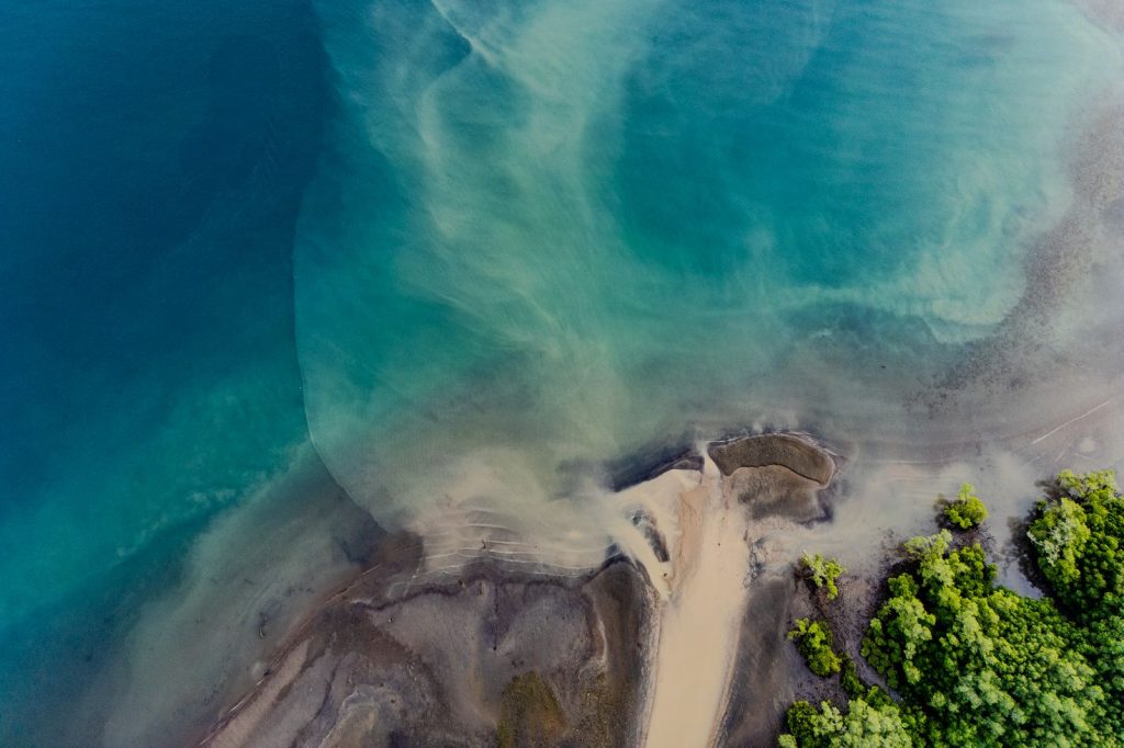 Aerial view of a tropical estuary where ocean currents mix coastal water, sand and mangroves.