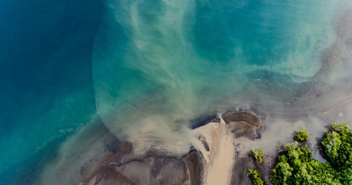 Aerial view of a tropical estuary where ocean currents mix coastal water, sand and mangroves.