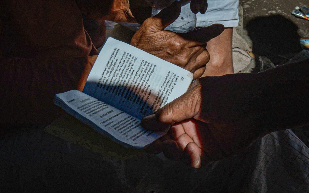 Hands holding a book written in a local language during a community reading.