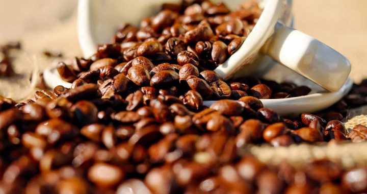 Roasted coffee beans spilled from a ceramic cup.