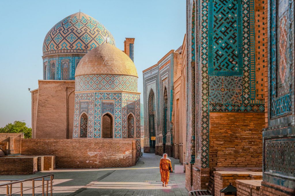 Personne marchant entre des bâtiments historiques décorés de mosaïques à Samarcande.