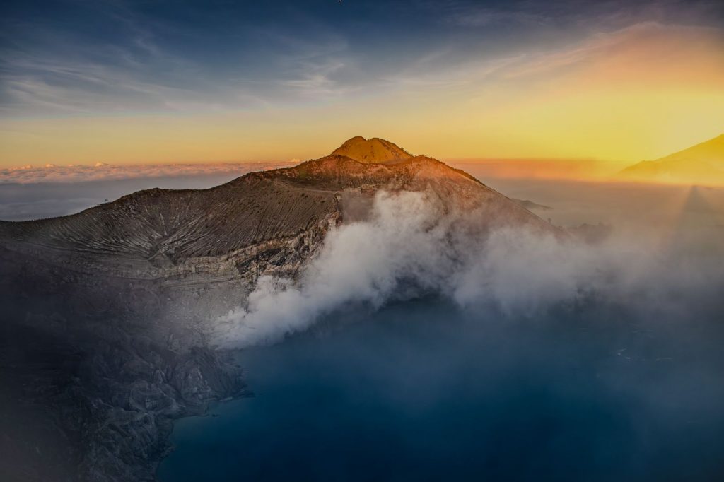 Sunrise over the Ijen volcano crater with volcanic fumaroles rising into the morning sky.