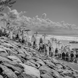 Balinese ceremonial procession descending to the sea beneath traditional umbrellas along the coast of Bali.