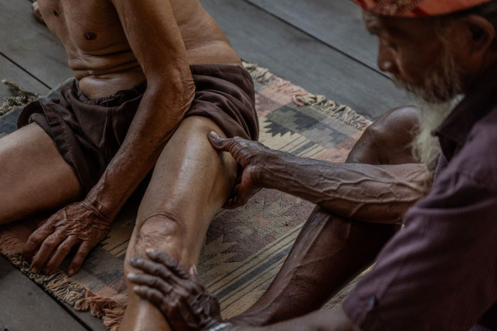 A Balinese healer applies pressure with his hands to a man's leg during a healing session in Bali.