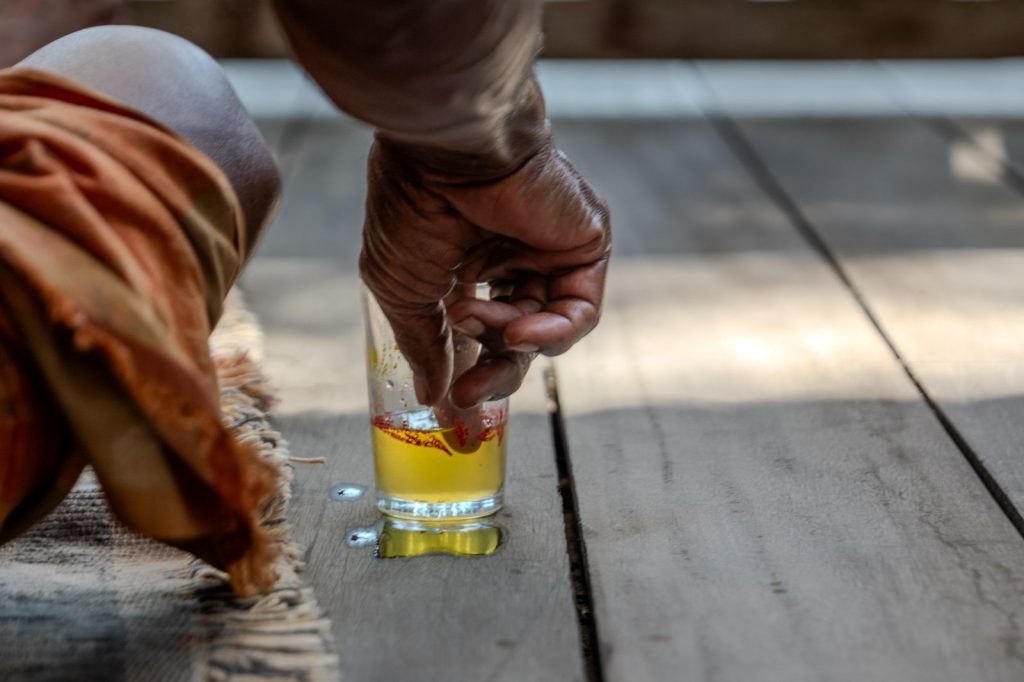 Hand of a practitioner dipping fingers into a glass containing a yellow oil used during a traditional treatment session.