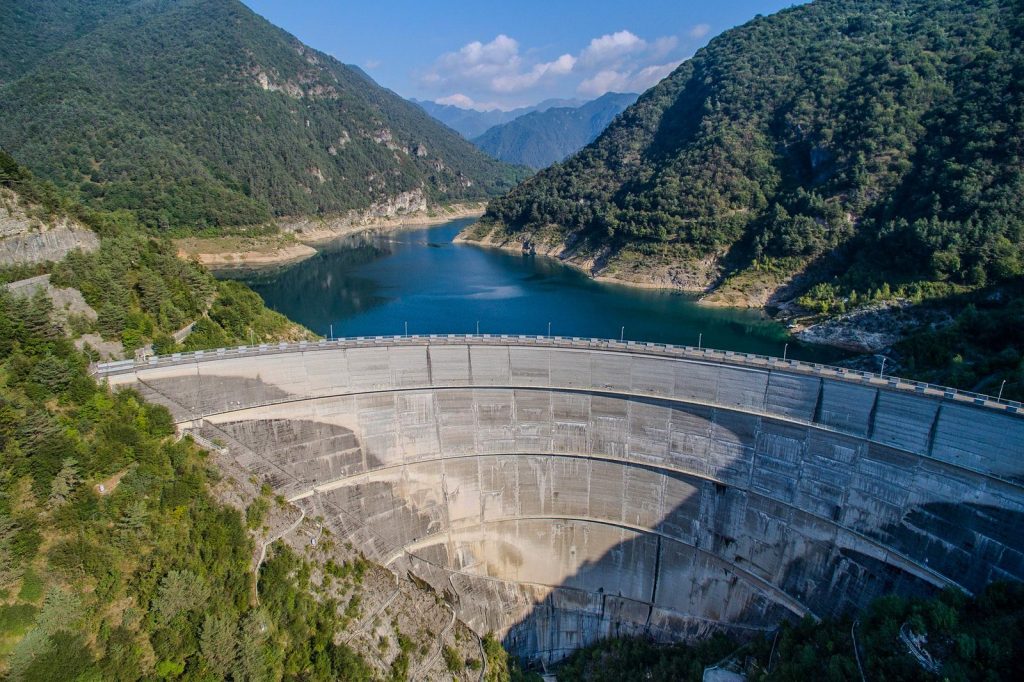Aerial view of a hydroelectric dam holding a reservoir between forested mountains.
