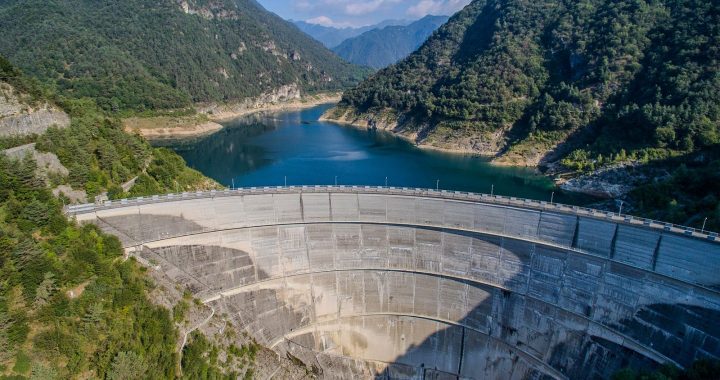 Aerial view of a hydroelectric dam holding a reservoir between forested mountains.