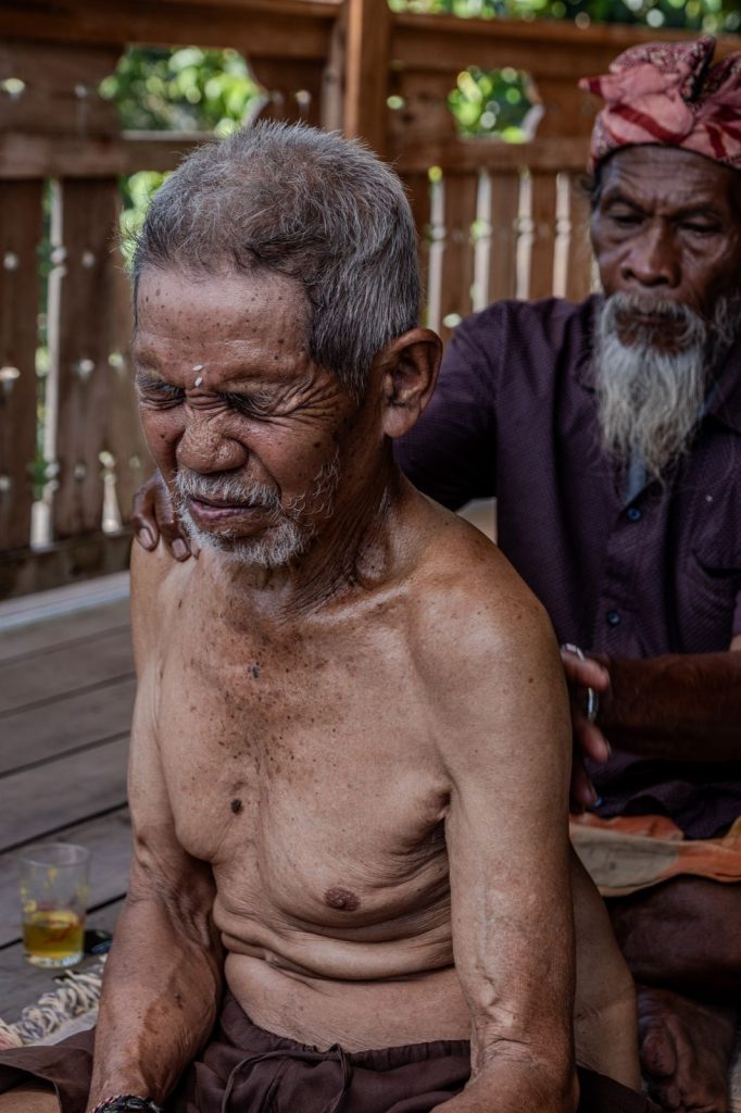 A man reacts to the pain while a Balian works on his back during a session.