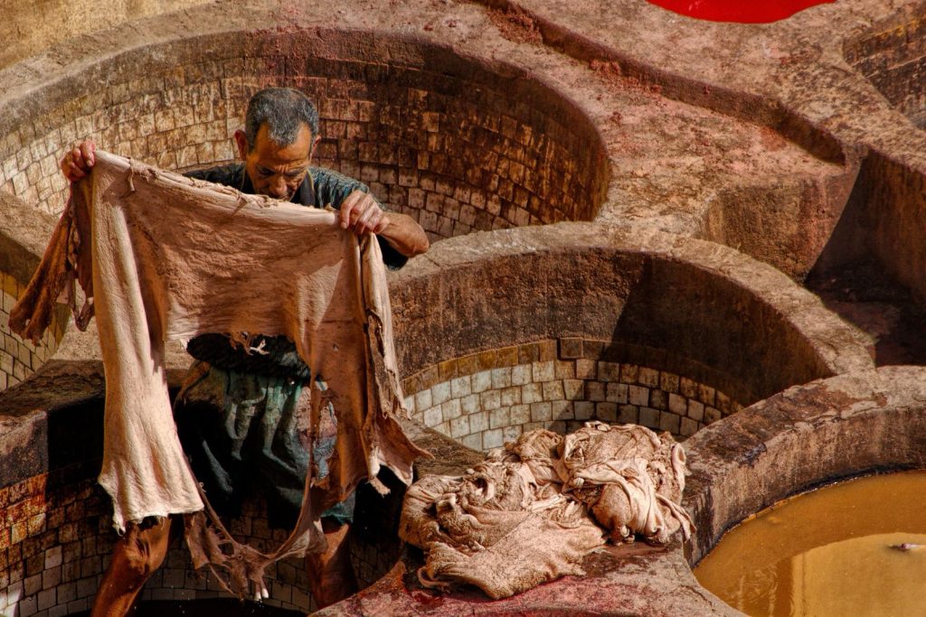 Un homme manipule une peau dans une tannerie traditionnelle entourée de cuves de traitement.