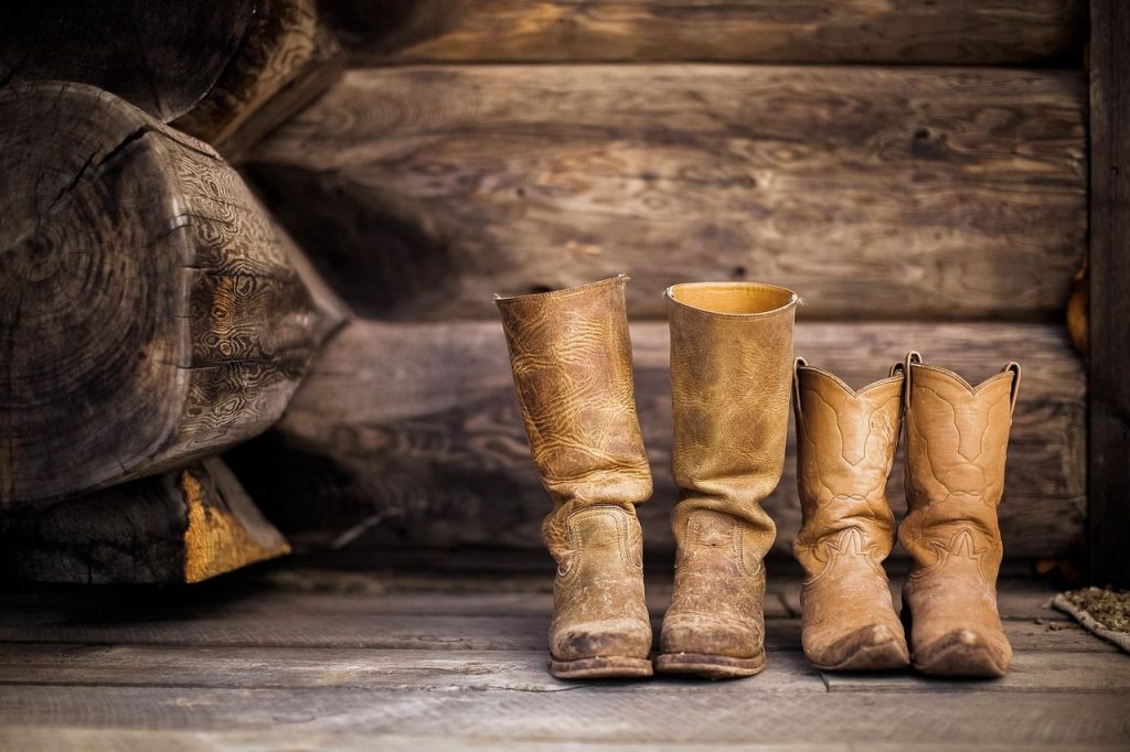 Deux paires de bottes en cuir usées posées côte à côte sur un plancher en bois.