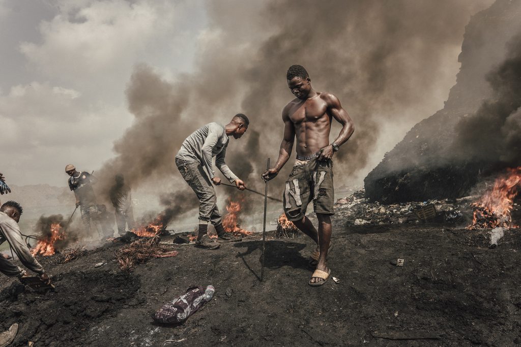 Men working amid burning waste and thick smoke, documented by photographer Manuela Federl.