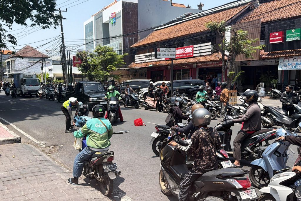 A police officer assists people involved in a motorcycle accident on a busy road in Bali, as traffic builds up around the scene.