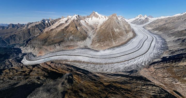 Aerial view of the Great Aletsch Glacier in the Swiss Alps, showing its curved ice flow, dark moraines and surrounding rocky mountains. Credit : © Rémih / Wikimedia Commons