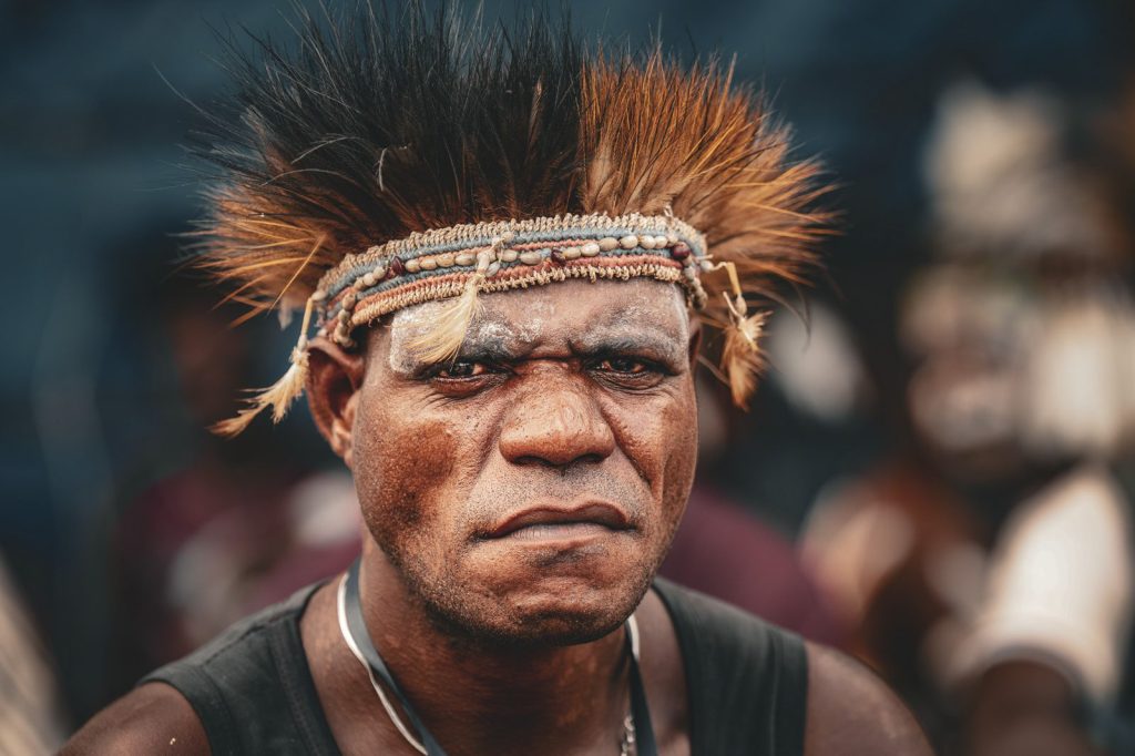 Portrait of a Papuan man wearing a traditional feather headdress and decorative headband.