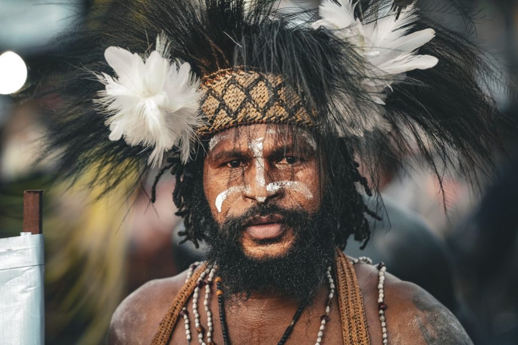 Papuan man wearing a traditional feather headdress and white face paint.