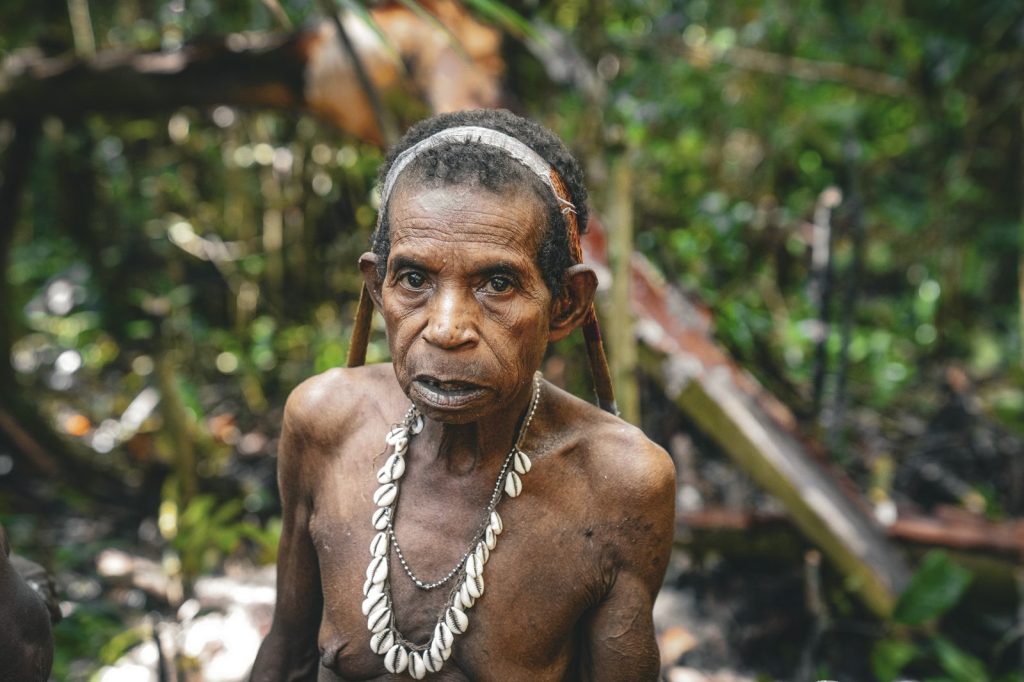 Papuan woman wearing a shell necklace while in a forest environment.
